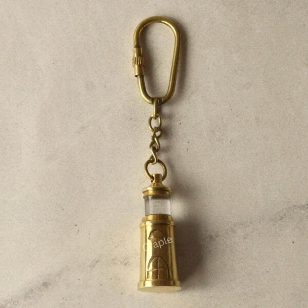 The miniature brass lighthouse keychain hanging from its secure carabiner clip against a neutral background.