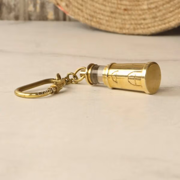 Close-up view of the brass lighthouse keychain on its side, focusing on the strong carabiner clip.