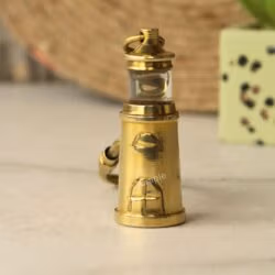 A clear, upright view of the detailed miniature brass lighthouse charm, showing its windows.