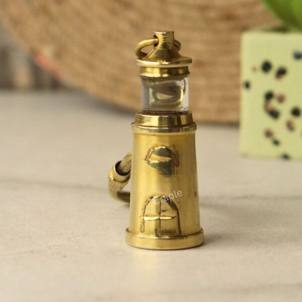 A clear, upright view of the detailed miniature brass lighthouse charm, showing its windows.