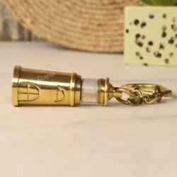 The full brass lighthouse keychain lying horizontally on a marble surface.