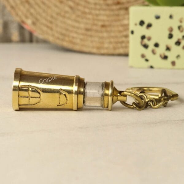 The full brass lighthouse keychain lying horizontally on a marble surface.