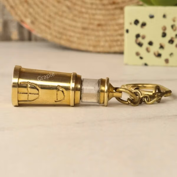 The full brass lighthouse keychain lying horizontally on a marble surface.