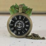 Antique brass 'Marine Anchor 1912' pocket watch with a black nautical dial, Roman numerals, and a matching chain.