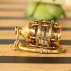 The brass miniature lantern keychain lying on its side, highlighting its sturdy, three-dimensional construction.