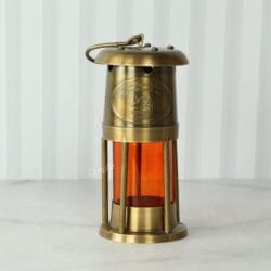 Front view of a vintage-style nautical miner's lantern with an antique brass finish and orange acrylic cylinder.