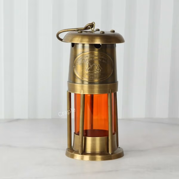 Front view of a vintage-style nautical miner's lantern with an antique brass finish and orange acrylic cylinder.