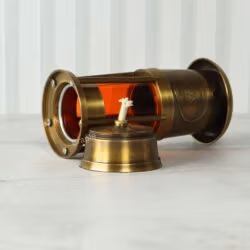 Nautical lantern lit with a warm orange glow, lying on its side with the brass oil lamp base visible.