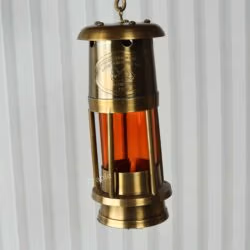 The antique brass miner's lantern hanging from its top D-ring handle, demonstrating its portability.