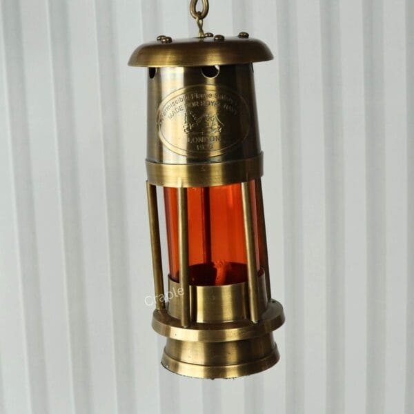 Orange Glow Nautical Lantern-7 The antique brass miner's lantern hanging from its top D-ring handle, demonstrating its portability.