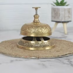 Ornate brass service bell with an engraved floral pattern and push-down plunger, for a hotel or reception desk.