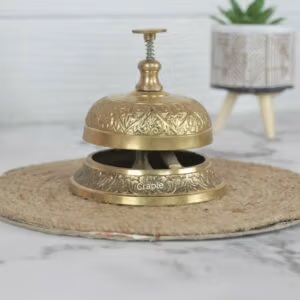 Ornate brass service bell with an engraved floral pattern and push-down plunger, for a hotel or reception desk.