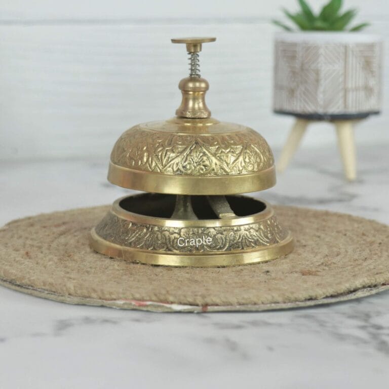 Ornate brass service bell with an engraved floral pattern and push-down plunger, for a hotel or reception desk.