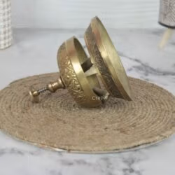 Disassembled ornate brass call bell showing the internal clapper mechanism and solid construction of the base and dome.