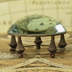 Antique brass desk magnifier and paperweight with a glass dome lens resting in a decorative gimbal stand on a vintage map.
