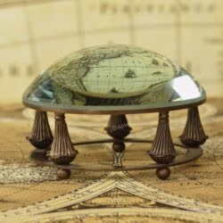 Antique brass desk magnifier and paperweight with a glass dome lens resting in a decorative gimbal stand on a vintage map.