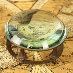 A close-up of the glass dome paperweight magnifier enlarging the details of an antique world map.
