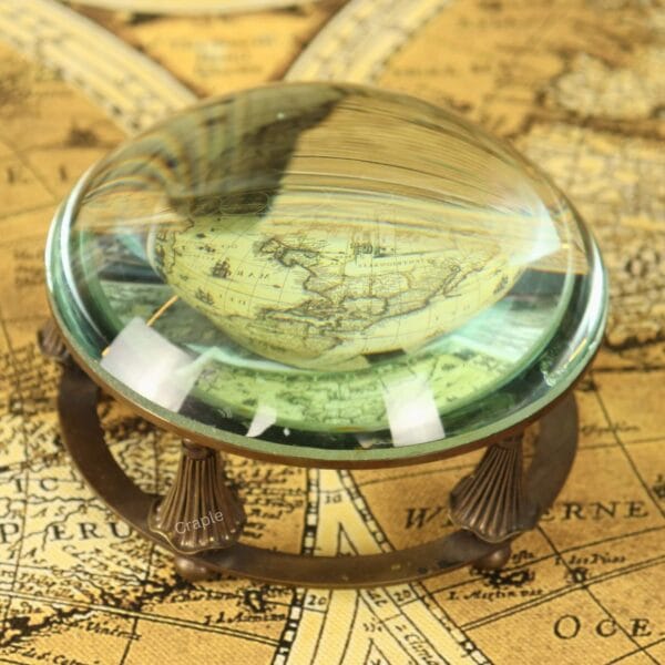 A close-up of the glass dome paperweight magnifier enlarging the details of an antique world map.
