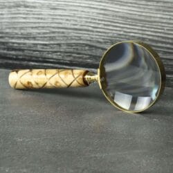 Vintage-style magnifying glass with a patterned wood handle and brass rim, standing upright on a dark surface.