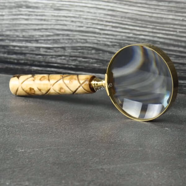 Vintage-style magnifying glass with a patterned wood handle and brass rim, standing upright on a dark surface.