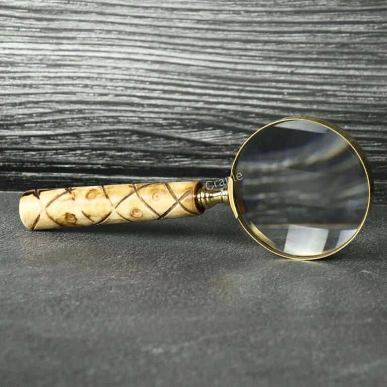 Handheld brass magnifying glass with a 5X lens and a patterned swirl wooden handle, resting on a slate tabletop.