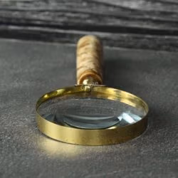Close-up of the 5X magnification lens and polished shiny brass rim of a handheld reading magnifier.