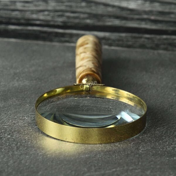 Close-up of the 5X magnification lens and polished shiny brass rim of a handheld reading magnifier.
