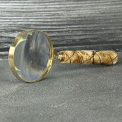 A brass and wood magnifying glass standing on its edge, showing reflections on its large lens.