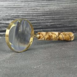 A brass and wood magnifying glass standing on its edge, showing reflections on its large lens.