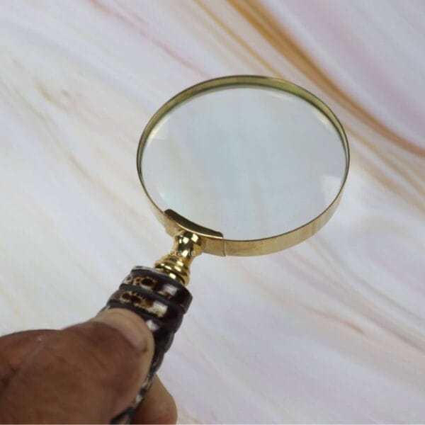 A person holding the vintage magnifying glass, showing the comfortable grip on the dark ribbed handle while viewing through the lens.