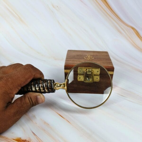 The 5X magnifying glass being used to examine the intricate brass latch on a small decorative wooden box.