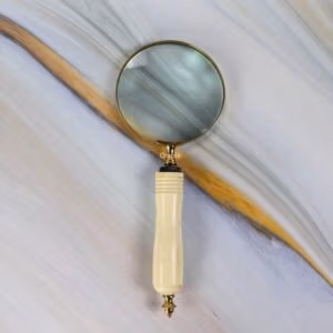 Vintage-style brass magnifying glass with a 5X lens and a carved, ergonomic bone-style handle against a marble background.