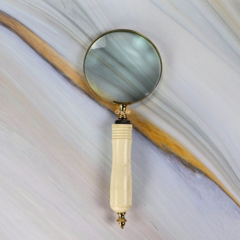 Vintage-style brass magnifying glass with a 5X lens and a carved, ergonomic bone-style handle against a marble background.