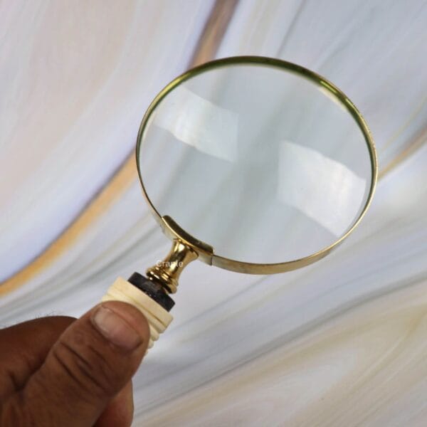 A hand holding the vintage magnifying glass, demonstrating the comfortable and ergonomic grip of its bone-style handle.