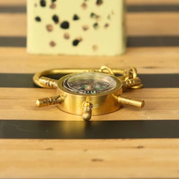 Side view of the solid brass shipwheel compass keychain, highlighting its sturdy, nautical design on a striped surface.