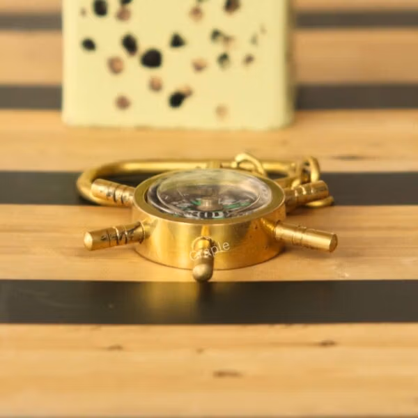 Side view of the solid brass shipwheel compass keychain, highlighting its sturdy, nautical design on a striped surface.