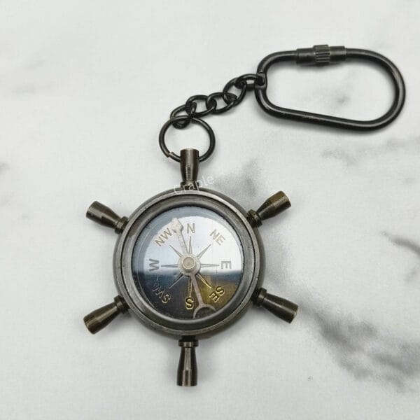 Functional shipwheel compass keychain with a white compass face and a black antique brass finish.