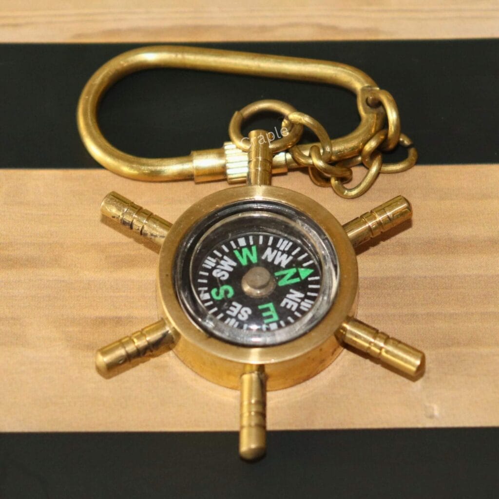 A functional brass shipwheel compass keychain with a shiny finish, showing the compass dial and secure carabiner clip.