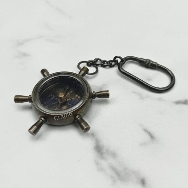 Angled view of the antique brass ship's helm compass keychain showing its solid construction.