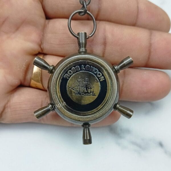 The antique brass shipwheel compass keychain held in a hand to show its pocket-friendly size.