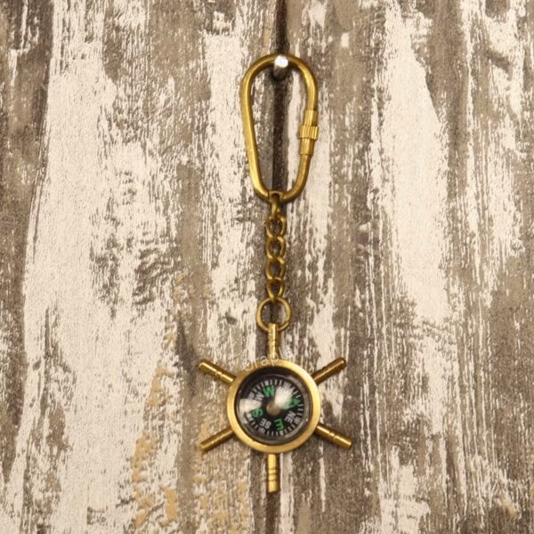 The nautical shipwheel compass keychain hanging from its brass carabiner clip against a rustic wood surface.