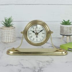 Golden aluminum desk clock with a classic white face and Roman numerals, displayed on a marble tabletop.