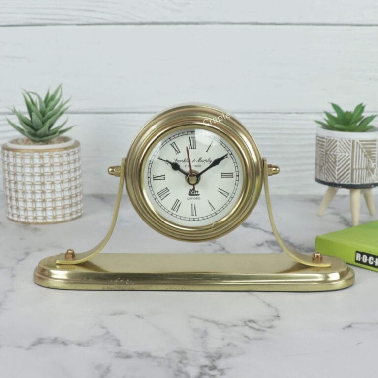 Golden aluminum desk clock with a classic white face and Roman numerals, displayed on a marble tabletop.