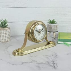 Angled side view of the golden tabletop clock, showing its curved stand and the depth of the clock case.