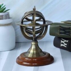 Small brass armillary sphere displayed as desktop decor next to a plant and vintage-style books.