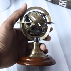A hand holding the small brass armillary sphere to demonstrate its compact, desktop size.