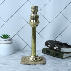 Stately brass Ashoka Pillar statue displayed on a desk next to books and a plant.