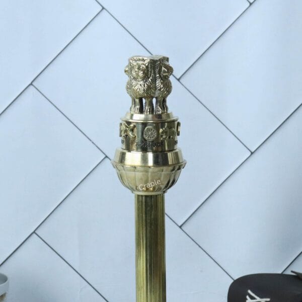 Side profile of the tall brass Ashoka Stambha (Pillar) showing its slender column and detailed Lion Capital.