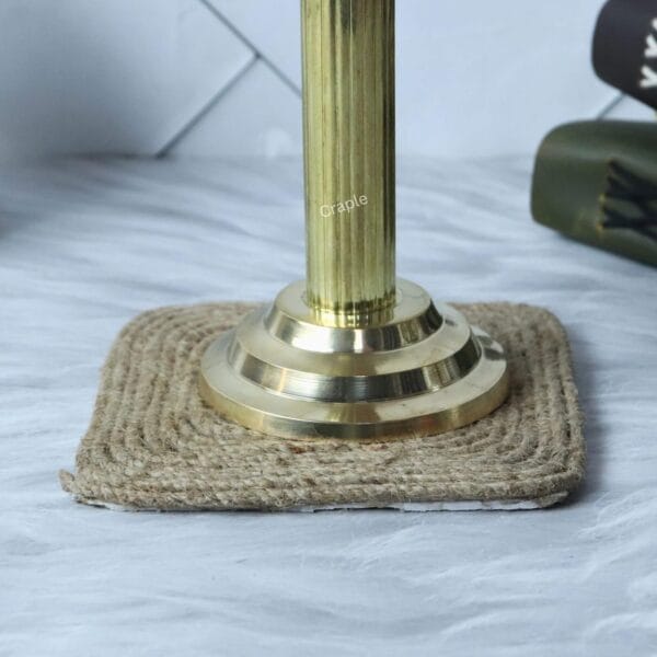 Close-up view of the sturdy, polished brass base of the Ashoka Pillar replica, resting on a jute coaster.
