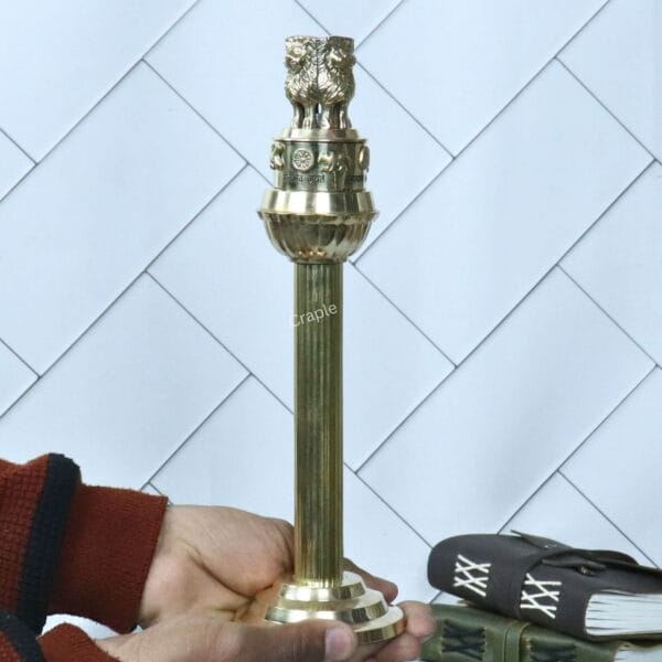 The brass Ashoka Pillar statue being held in a hand to demonstrate its size and scale.